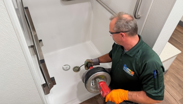 Professional shower drain cleaning service in Champaign, IL. Plumber using a drain snake to clear a clogged shower drain.