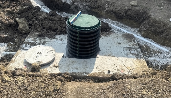 Septic Tank Installation Partially buried residential septic tank installation with access riser and concrete lids, surrounded by dirt and gravel trenches
