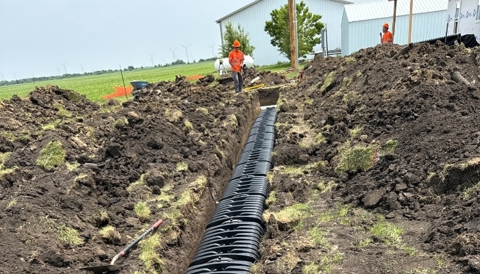 Leach Field Installation Workers installing a black chamber-style leach field system in a long excavated trench on a residential property
