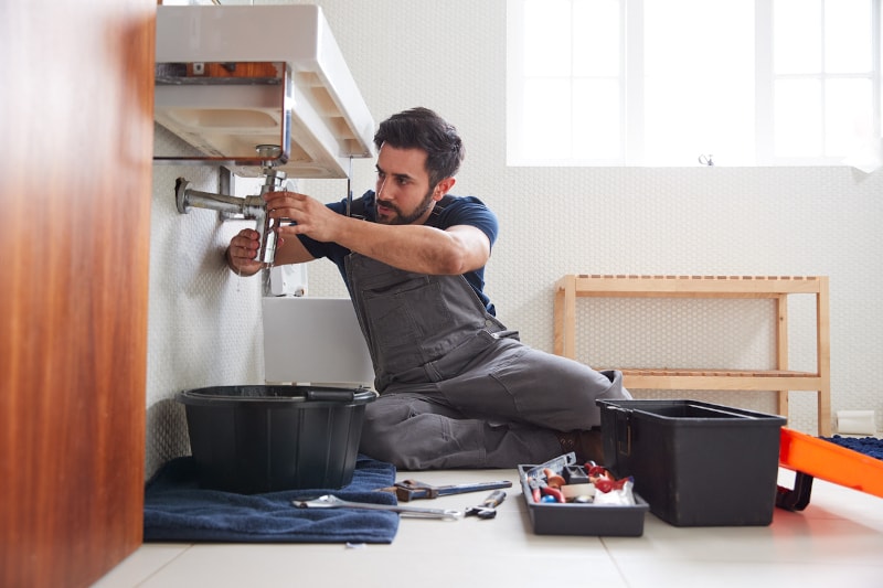 male plumber working to fix leaking sink min