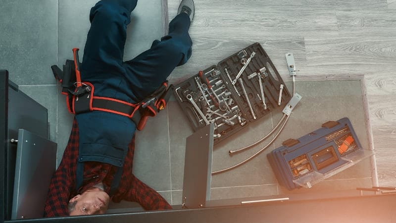 plumber laying on his back next to tool set fixing sink