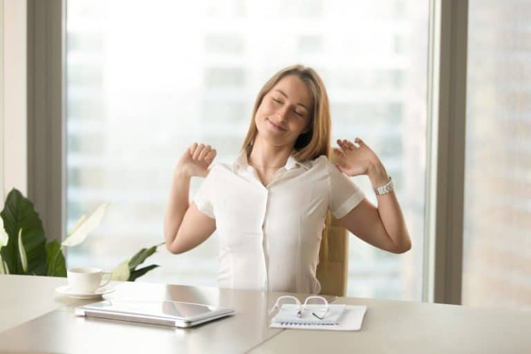 woman stretching and smiling while sitting at a desk min